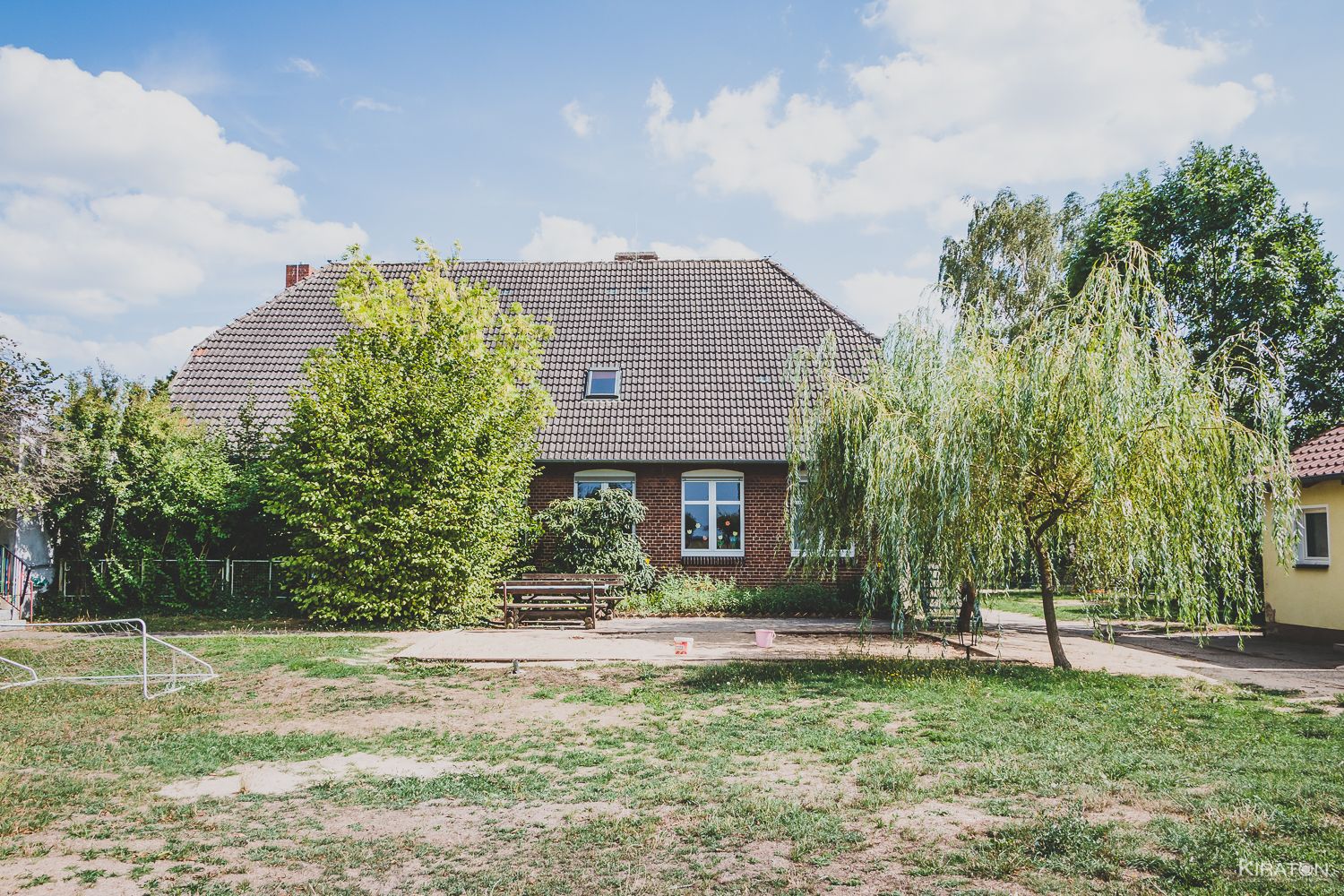 verwunschen wirkendes Landhaus aus Backstein mit Bäumen und Wiese davor.